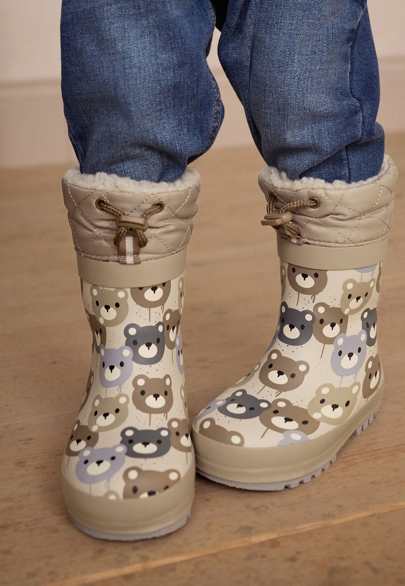 Bottes de pluie en caoutchouc couleur crème avec un motif d'ours en marron et bleu. Col en tissu matelassé beige avec cordon de serrage pour un ajustement personnalisable.