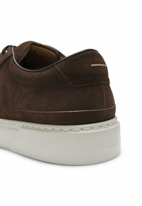 Baskets en daim marron avec bordure noire et semelle blanche épaisse, montrant le talon arrière et le nom de la marque embossé sur la semelle.