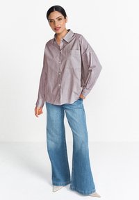 Striped button-up shirt in light brown and white, featuring a chest pocket. Paired with wide-leg blue jeans and pointed white shoes.