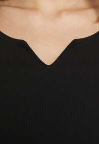 Mustikka ribbed-paita, jossa on V-kaula-aukko, korostaen sen tekstuurista kangasta ja tiukkaa siluettia.