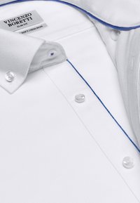 Chemise blanche slim fit avec un tissage texturé, dotée de piping bleu le long du col. Comprend quatre boutons blancs sur la patte de boutonnage.