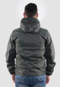 Giacca leggera di colore verde scuro con cappuccio, polsini elasticizzati e una texture liscia e lucida. Presenta una ventola posteriore e un orlo aderente.