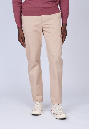Pantalon en coton beige à coupe droite, doté de poches latérales et d'une texture lisse, associé à des baskets en toile blanches.