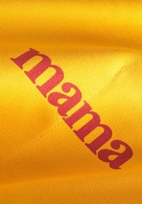 Gul tyg som har ordet "mama" tryckt i fet röd text. Materialet har en strukturerad yta med synliga vävda mönster.