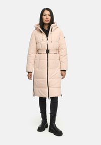 Light pink puffer coat with a belted waist, zip closure, and hood. Features quilted texture and black accents. Worn with black skinny jeans and boots.
