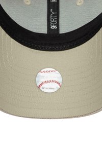 Beige Baseballcap mit schwarzem Schirm. Mit einem runden weißen Aufkleber mit rotem Baseballstich. Texturiertes Material und verstellbares Innenband.