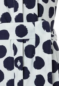 Marineblau- und weiße Bluse mit Punkten, die über einen Knopfverschluss, einen Gurt in der Taille und einen Baumwollstoff mit strukturiertem Finish verfügt.