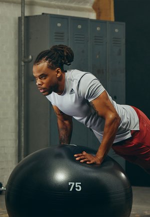 Black exercise ball with the number "75" on it, matte finish; person in gray athletic shirt and red shorts performs push-ups on it.