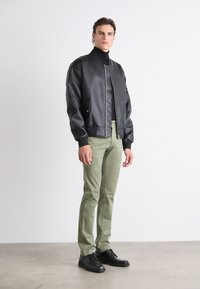 Černá kožená bomber bunda s ribbovanými náplety, zipovým zapínáním a dvěma postranními kapsami, spárovaná se zelenými kalhotami a černými botami.