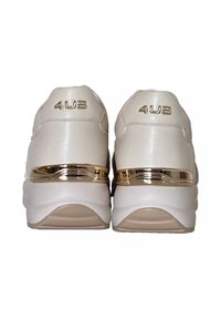 Sneakers beige con logo dorato "4US" sul tallone e una banda dorata riflettente sopra la spessa suola bianca, mostrati da dietro.