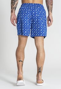Blå badshorts med tryck av vitt logotyp över hela. De har en elastisk midja och sidofickor. Tillverkade av lätt och snabbtorkande material.