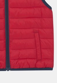 Czerwona kamizelka z podszewką, zapinana na zamek błyskawiczny, z boczną kieszenią i granatowymi wykończeniami. Posiada pikowane sekcje oraz miękką, gładką teksturę.