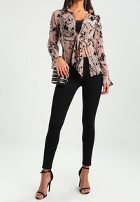 Blusa trasparente a stampa serpente in tonalità blush, con maniche lunghe e dettaglio con fiocco davanti, abbinata a jeans skinny neri e tacchi neri con cinturini. Accessorio bag nera.