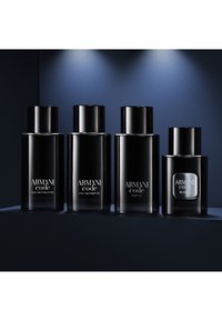 Cuatro botellas negras de fragancia Armani Code en fila, etiquetadas como Eau de Toilette, Eau de Parfum, Parfum y Elixir, sobre una superficie oscura con un foco de luz.