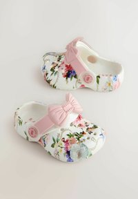 Lillelise, valge alusega lillemustrilised puukingad, millel on roosa keerutussang; valmistatud paindlikust materjalist ventilatsiooniaukudega.