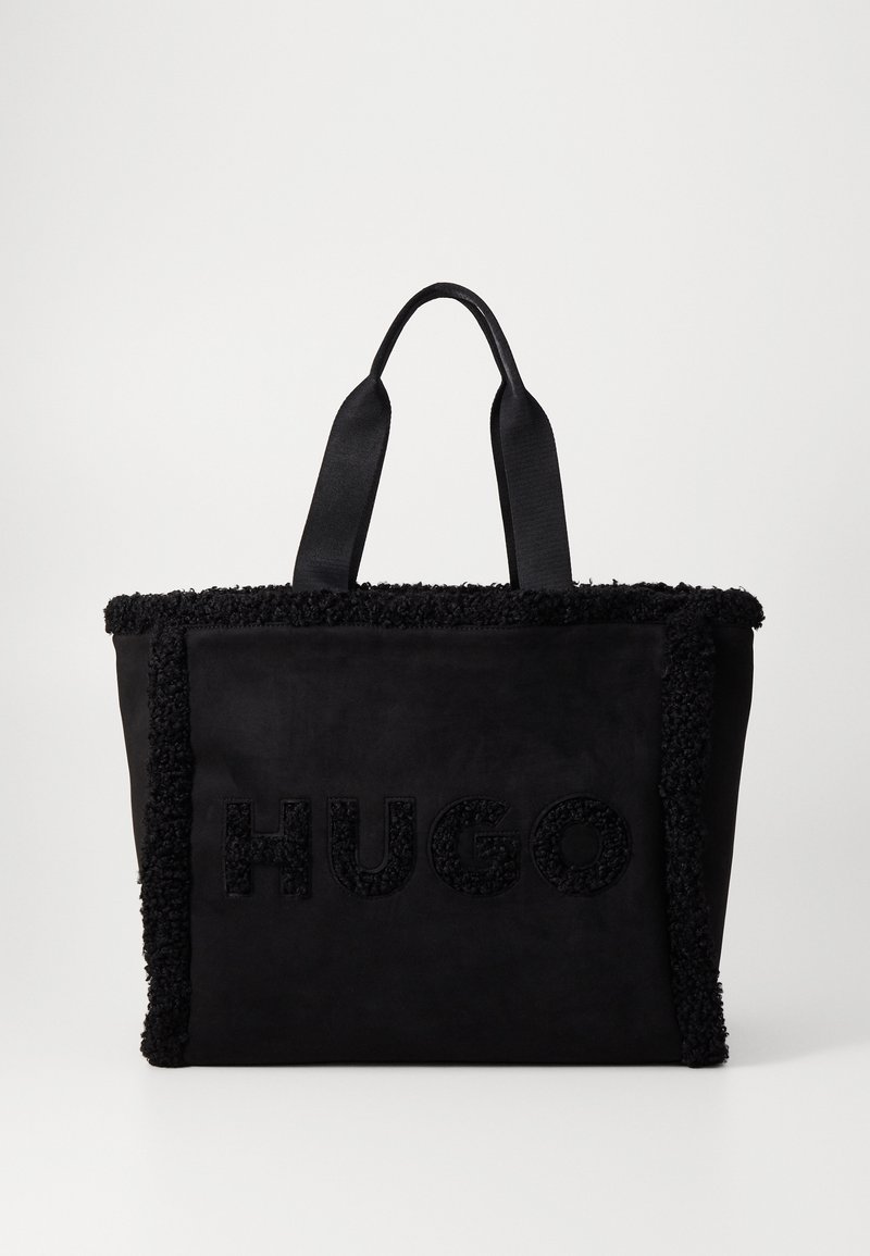 Sac fourre-tout noir présentant une texture douce, des détails en franges le long des bords, et un logo HUGO embossé sur le devant. Poignées en forme de selle.