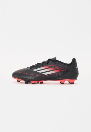 Chaussure de football noire avec accents rouges, présentant une tige texturée, un design épuré et six crampons moulés pour la traction.