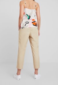 Haut sans manches léger à motif floral en blanc et couleurs pastel, associé à un pantalon beige à coupe décontractée et des baskets blanches.