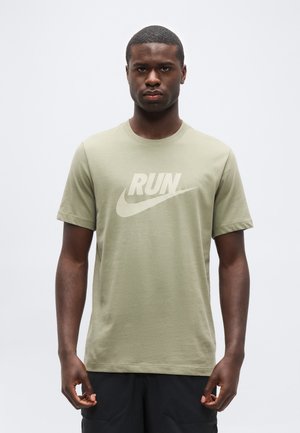 Čierny muž stojaci čelom dopredu, oblečený v svetlozelenom tričku s nápisom „RUN“ a znakmi Swoosh v svetlej potlači na hrudi.