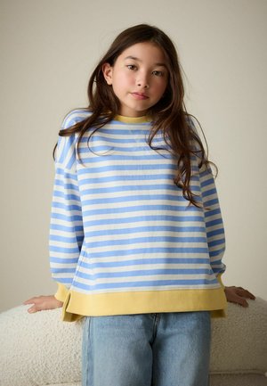 Stribet pullover i lyseblå og creme med gule manchetter. Har en afslappet pasform og blød tekstur. Kombineret med lyseblå cowboybukser.