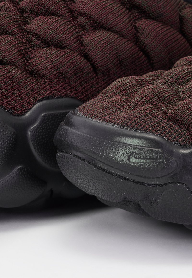 Bordowe dzianinowe buty sportowe z teksturowaną powierzchnią, z czarną gumową podeszwą i małym wytłoczonym logo po boku.