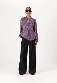 Purple floral patterned blouse with a mandarin collar, paired with loose dark denim pants. Model wears sunglasses and simple earrings.