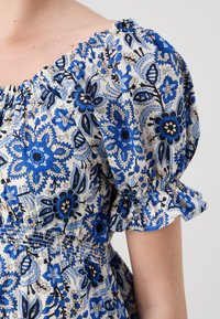 Φλοράλ φόρεμα με μπλε και μαύρο μοτίβο σε ανοιχτό φόντο, με φουσκωτά μανίκια, σφηκοσώμη και βολάν στις άκρες των μανικιών.