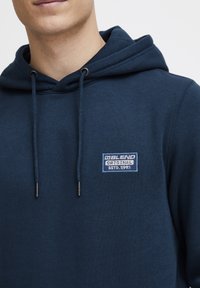 Felpa blu navy realizzata in tessuto morbido, con tasca a marsupio, coulisse e una toppa con il logo con la scritta "Blend Original".