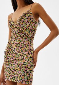 Blommig klänning med svart bakgrund, livfulla rosa, orange och gula blommor; volangad halsringning; kroppsnära passform; justerbara axelband.