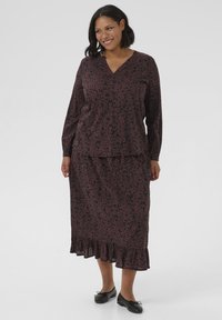 Haut à motifs floraux noir et bordeaux avec un décolleté en V et des manches longues, associé à une jupe assortie avec un ourlet en volants. Balances noires.