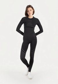Zwart atletisch top met lange mouwen en legging met subtiele naadtoevoegingen. Gemaakt van rekbaar materiaal ontworpen voor beweging en comfort.