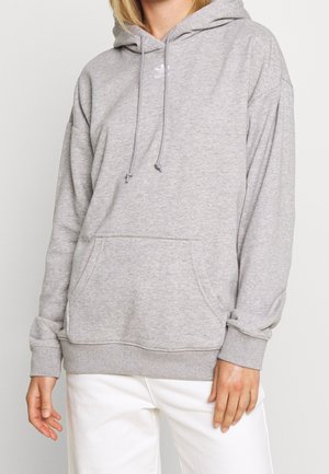Sweatshirt à capuche gris en tissu doux, avec une poche frontale, des cordons de serrage et un petit logo sur la poitrine.