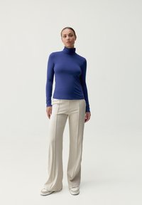 Långärmad polotröja i mörkblått, tillverkad av slät tyg, kombinerad med beige vida byxor och vita sneakers.