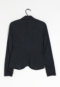 Blazer nero con maniche lunghe, rever a punta e design aderente. Presenta un orlo curvo e dettagli delle cuciture verticali sulla schiena.