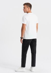 Vit bomull t-shirt med korta ärmar, parat med svarta denim-jeans. Outfiten kompletteras med vita sneakers och en svart armbandsklocka.