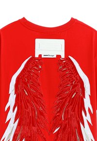 Camiseta roja con diseños de alas bordados en blanco y dorado en la parte posterior, con una etiqueta rectangular blanca en el cuello.