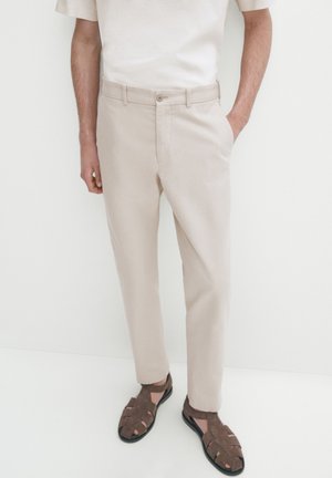 Lichtbeige broeken met een gladde textuur, rechte pasvorm, voorzakken en een bijpassende riem. Gepaard met bruine, gestrikte sandalen.