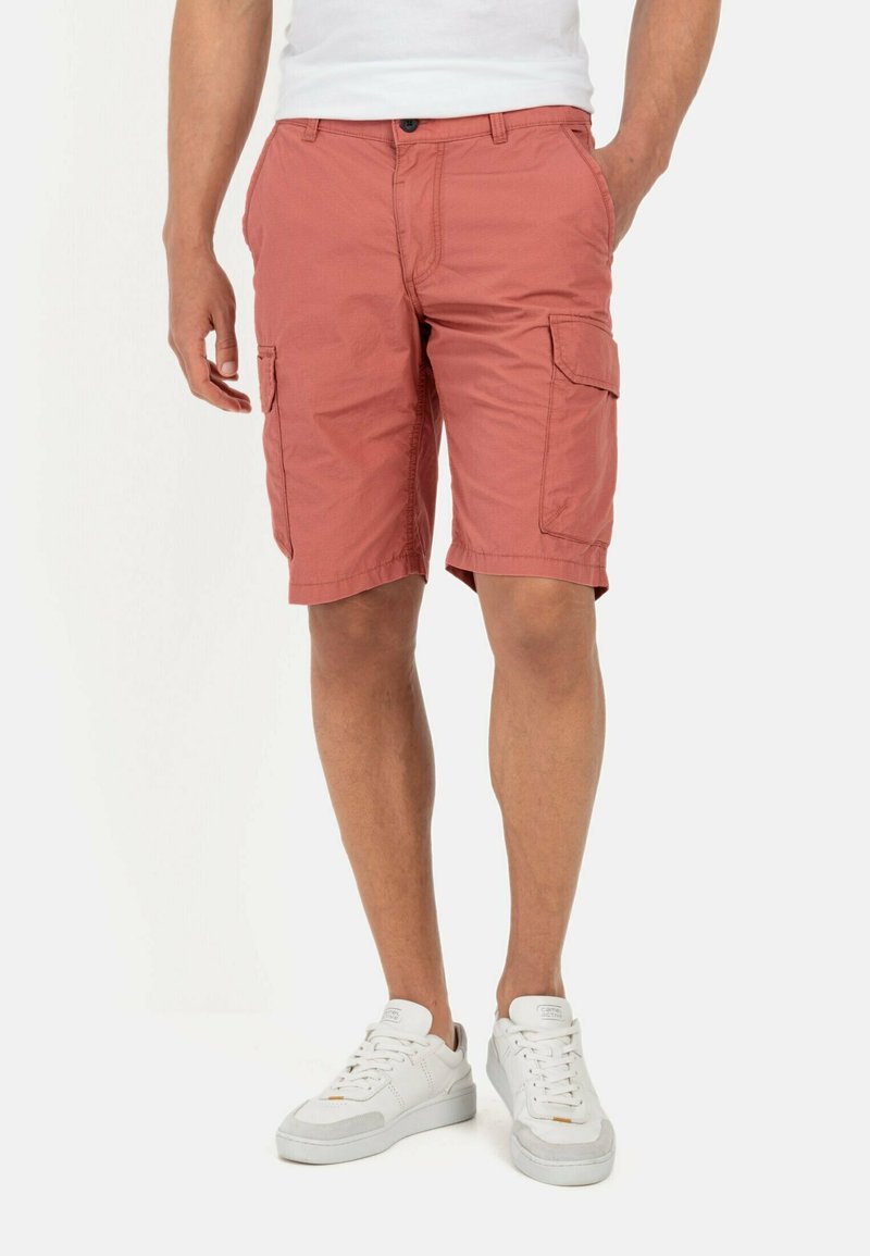 Cargo-Shorts in verblichenem Korallenrot mit zwei seitlichen Taschen, einem Knopfverschluss und lockerer Passform, kombiniert mit weißen Sneakern.