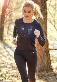 Black long-sleeve athletic shirt featuring a panther graphic with blue eyes, paired with black leggings, suitable for running in a wooded area.