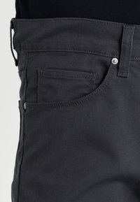 Schwarze Denim-Jeans mit einer Vordertasche, silberner Hardware und strukturierter, glatter Oberfläche.