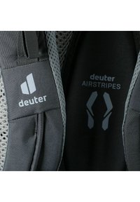 Correas de malla gris con el logo 'deuter' y el texto 'AIRSTRIPES'. Tela texturizada contra un forro interior liso, con detalles de forma ergonómica.