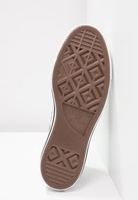 Braune Gummisohle mit einem geometrischen Profil, weißem Besatz und dem "Converse All Star"-Logo. Robustes und strukturiertes Design.