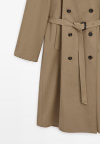 Beiger, doppelreihiger Trenchcoat mit tailliertem Gürtel, großen schwarzen Knöpfen und einem glatten, strukturierten Stoff. Weite Ärmel und mittellange Länge.