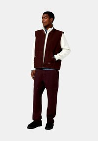 Chaleco burdeos sobre una chaqueta crema, combinado con pantalones burdeos a juego. Cuenta con cierre de cremallera, bolsillos frontales y tejido texturizado. Zapatos negros.