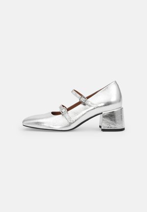 Srebrne metaliczne buty Mary Jane z dwoma paskami z klamrami i niskim obcasem typu block, pokazane z profilu na białym tle.