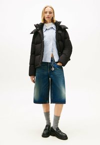 Zwarte gewatteerde jas, lichtblauw gestreept shirt, denimm culottes, grijze sokken en zwarte loafers met dikke zolen, met een sleutelhangerdetail.