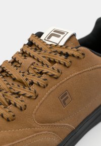 Zapatillas de ante marrón con cintas a rayas negras y marrones, que cuentan con una suela de goma negra y un parche de logo blanco en la lengüeta.