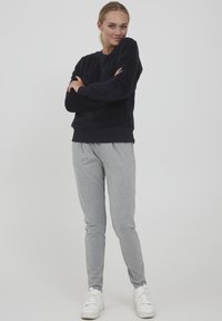 Laivansinis pehmeä huppari ribatulla hihalla, yhdistettynä vaaleanharmaisiin slim-fit-collegehousuihin ja valkoisiin tennareihin neutraalilla taustalla.