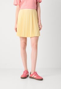 Gonna gialla plissettata con una vita aderente, abbinata a sneakers rosa con texture in suede e strisce bianche di accento.