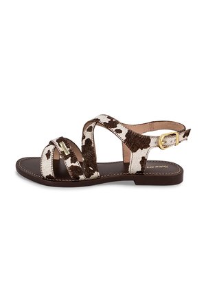 Sandalias con estampado de vaca en marrón y blanco, con diseño de correas cruzadas, cierre con hebilla y suela plana marrón. Parte superior texturizada y detalles cosidos.